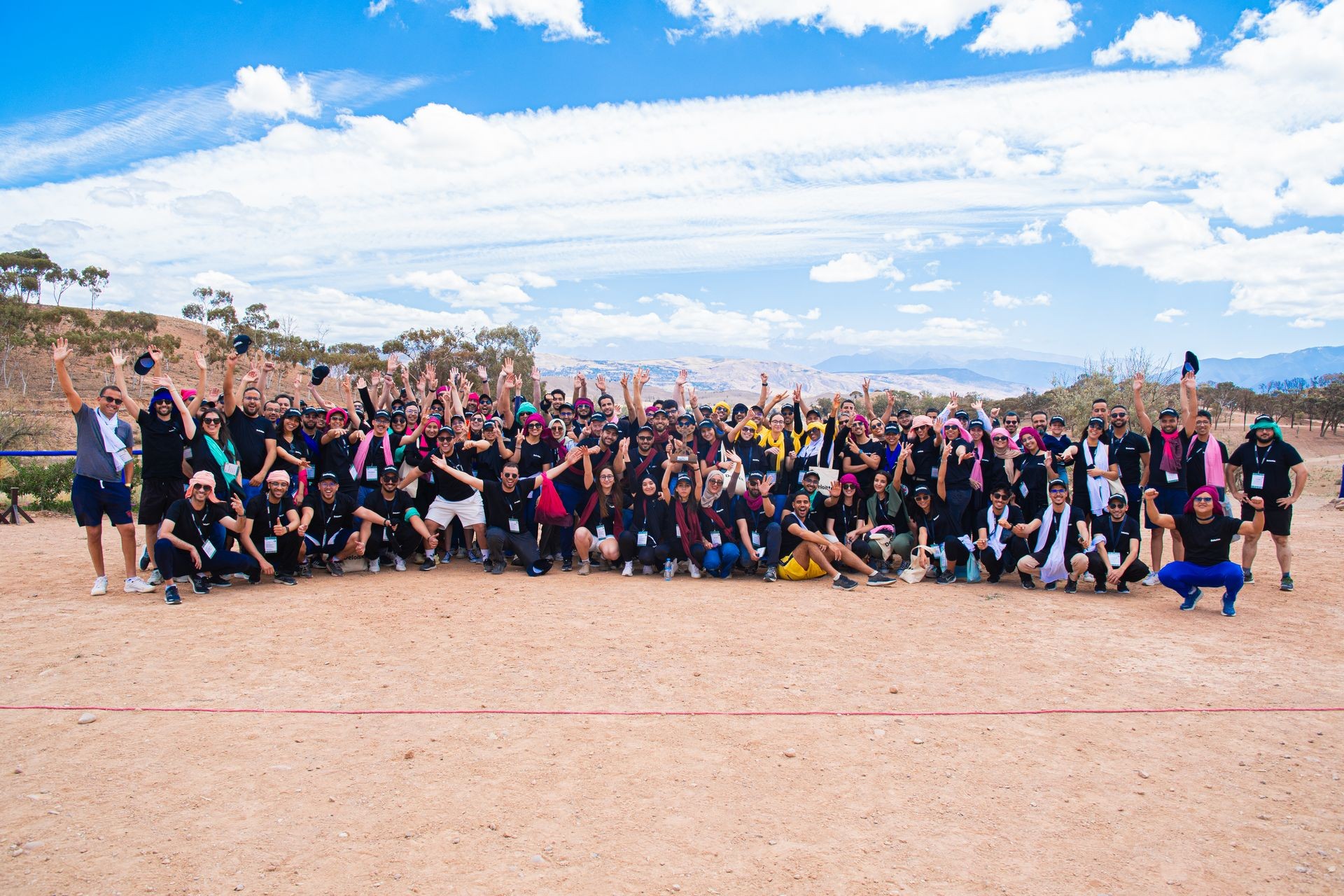 Group of people posing together outdoors on a sunny day with a clear blue sky and distant mountains.