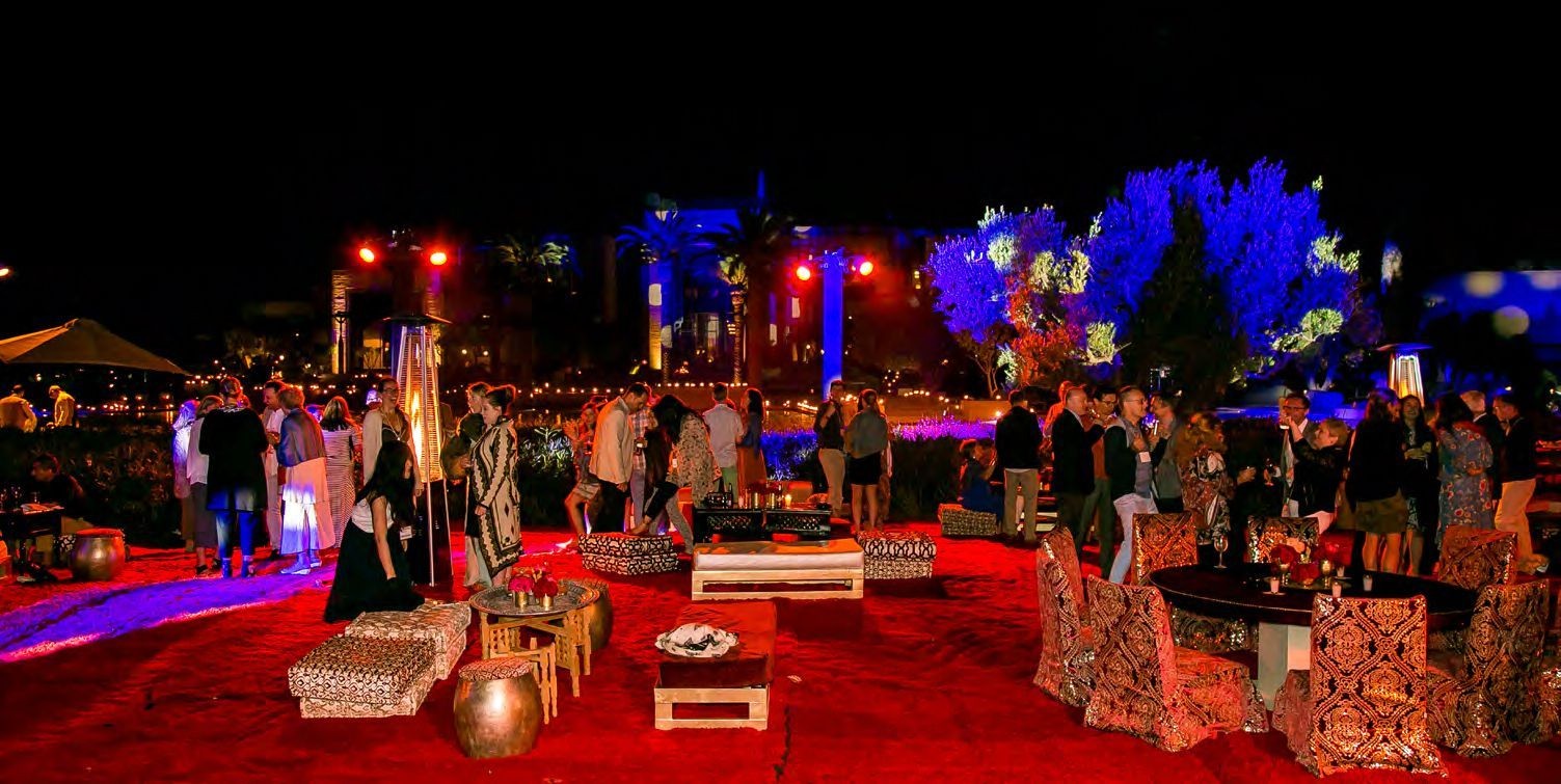 Outdoor evening gathering with people socializing, surrounded by colorful lights and decorated seating.